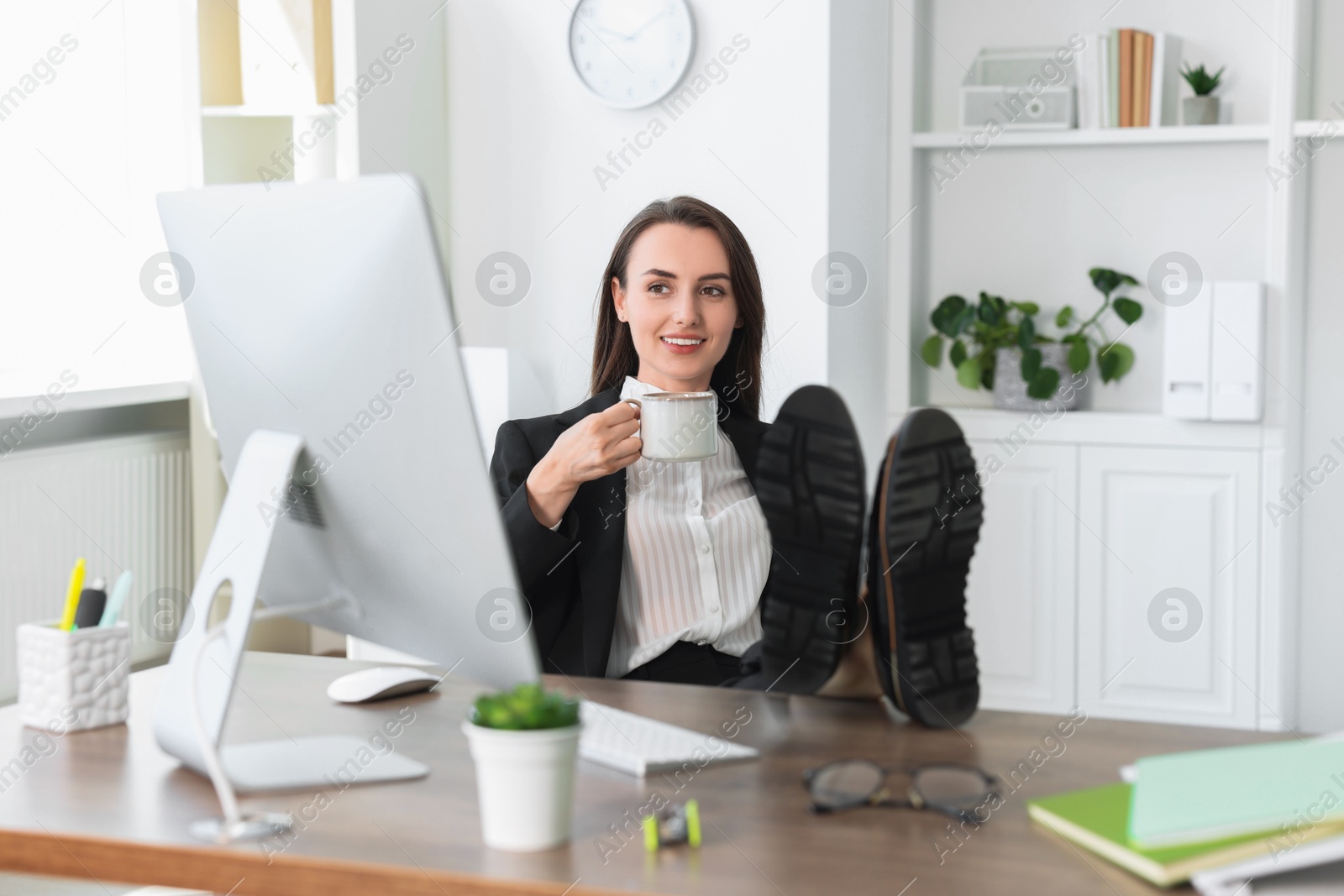 Photo of Smiling businesswoman drinking coffee holding legs on table in office. Break time