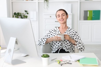 Photo of Smiling businesswoman drinking coffee at table in office. Break time