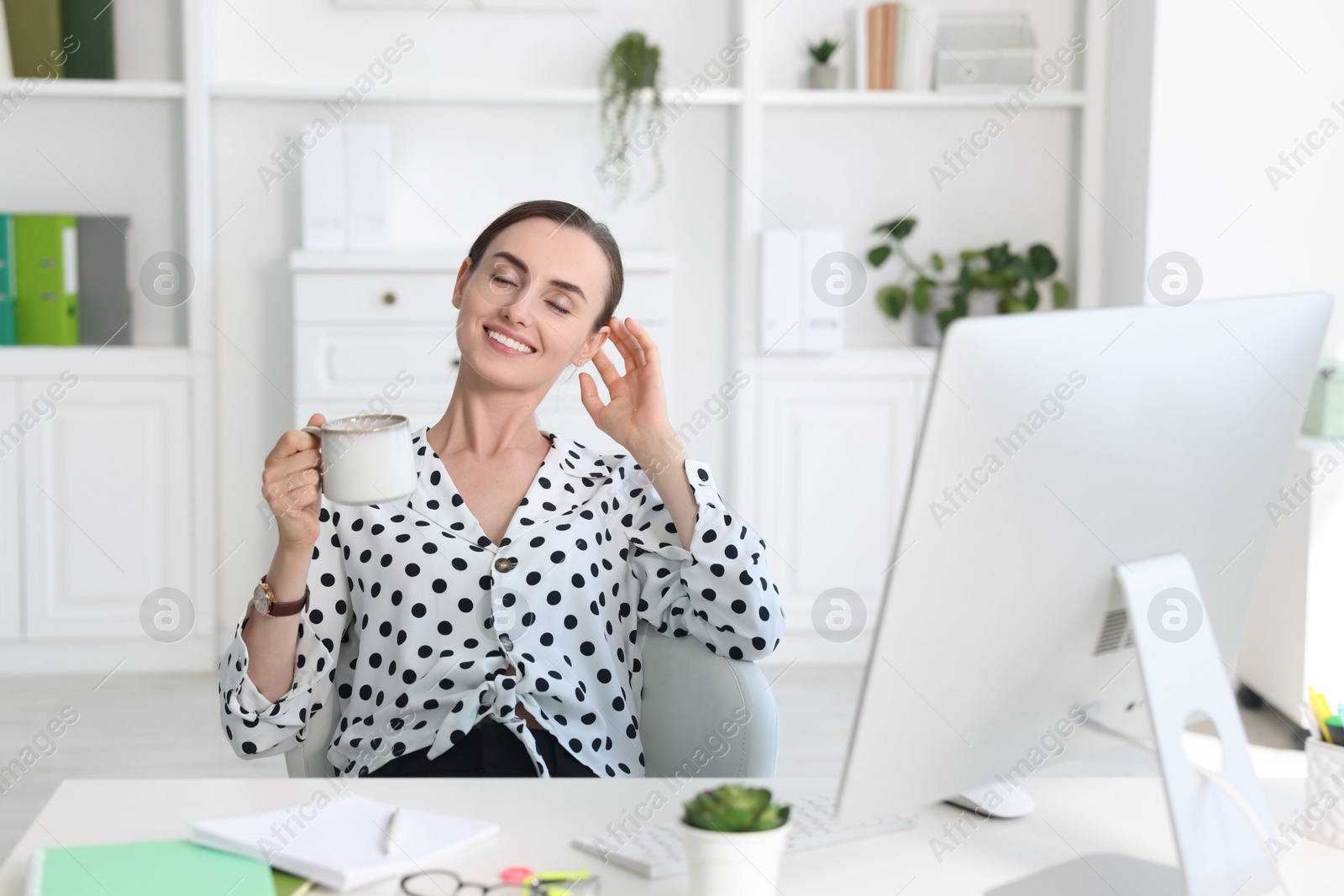 Photo of Smiling businesswoman drinking coffee at table in office. Break time