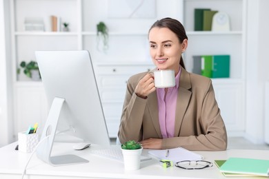 Photo of Smiling businesswoman drinking coffee at table in office. Break time