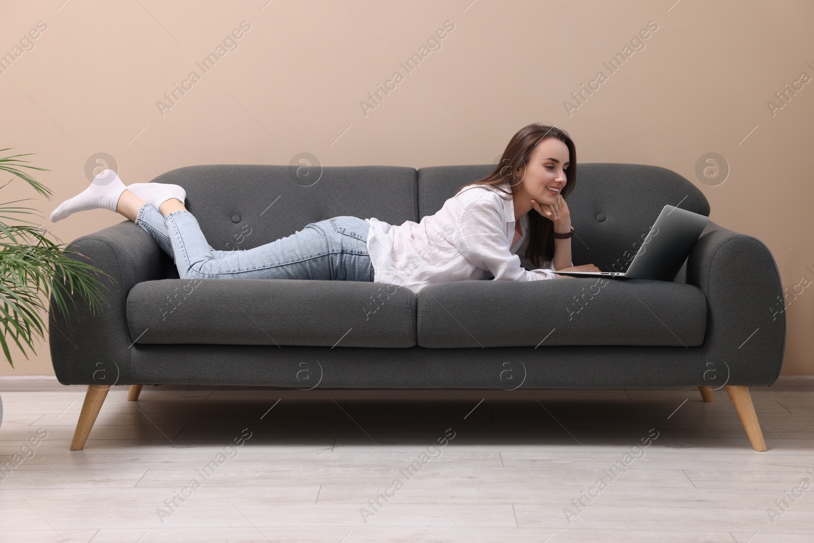 Photo of Smiling woman with laptop lying on sofa at home