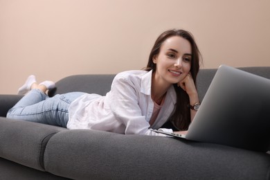 Smiling woman with laptop lying on sofa at home