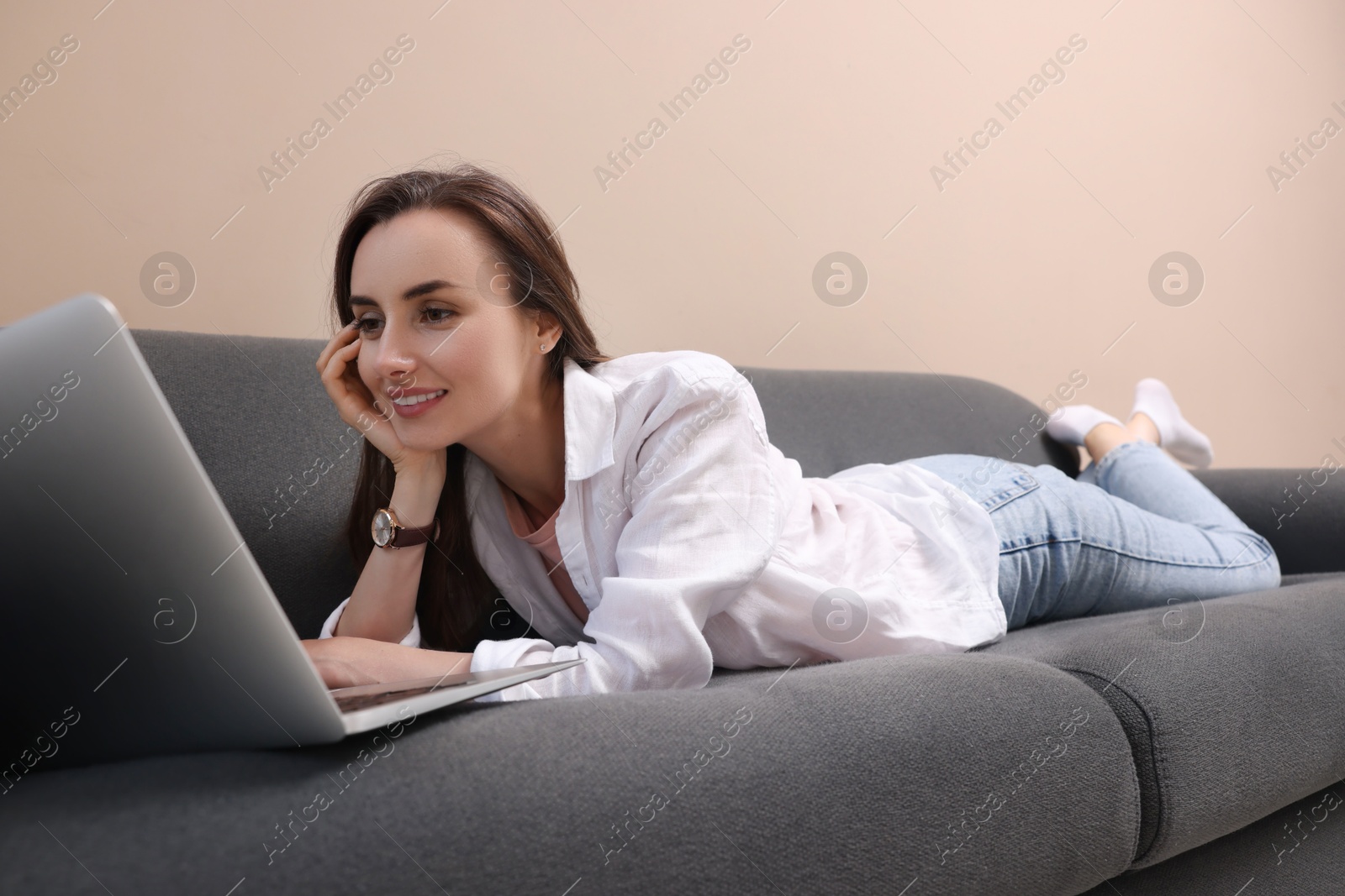 Photo of Smiling woman with laptop lying on sofa at home