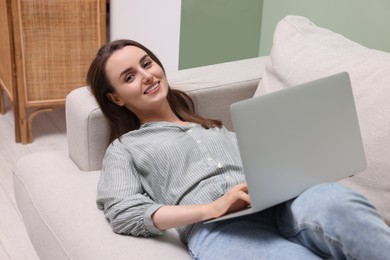 Photo of Smiling woman with laptop lying on sofa at home