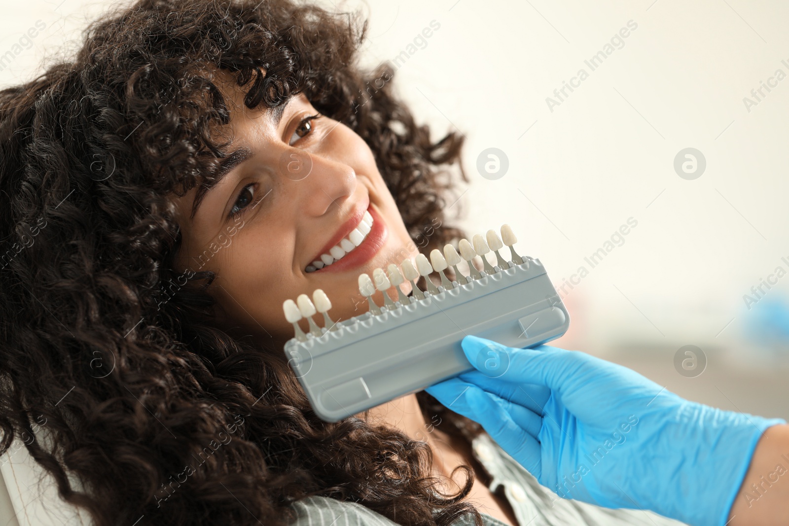 Photo of Doctor checking young woman's teeth color in clinic, closeup. Dental veneers