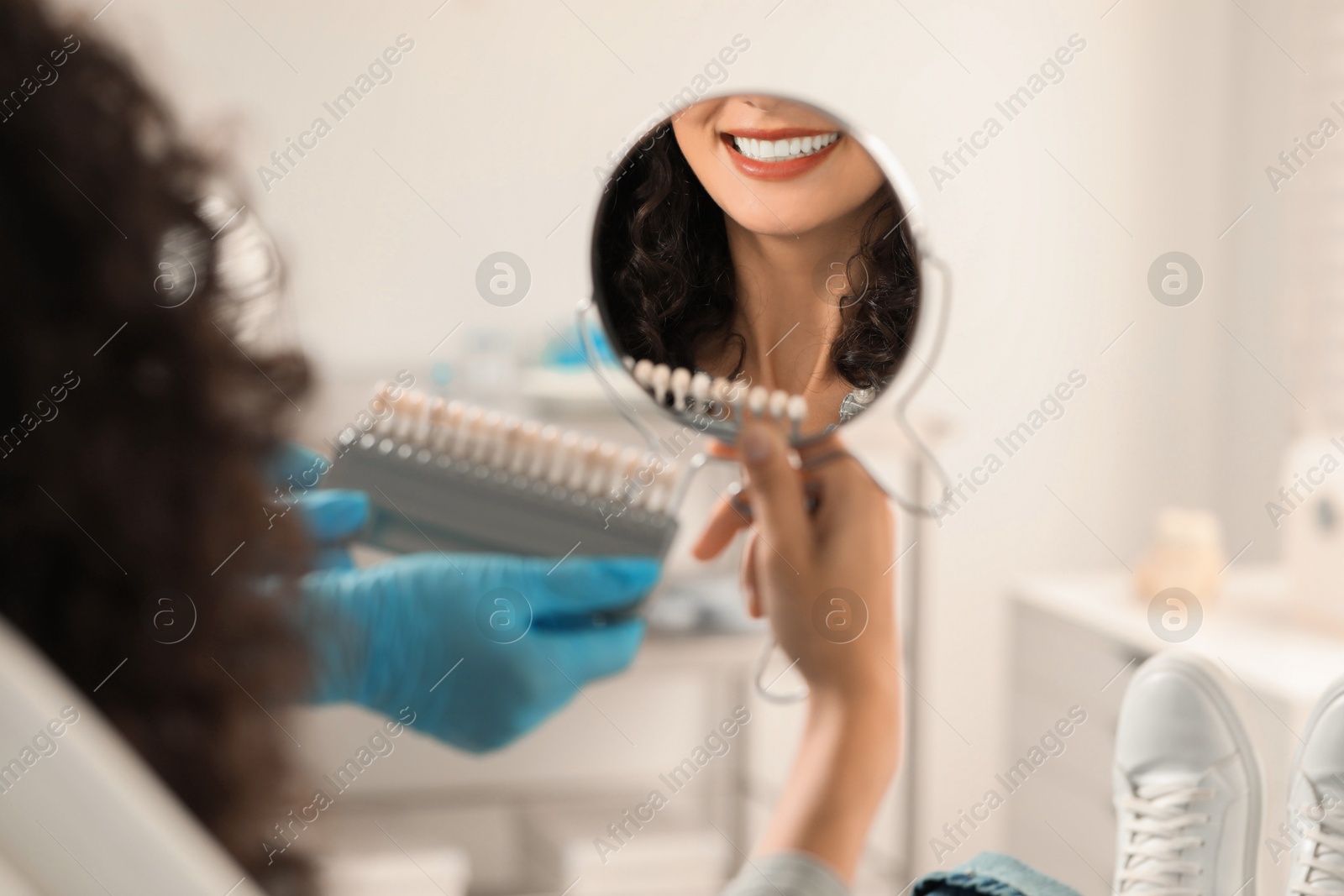 Photo of Patient looking in mirror while doctor holding teeth color chart in clinic, closeup. Dental veneers