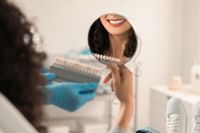 Patient looking in mirror while doctor holding teeth color chart in clinic, closeup. Dental veneers