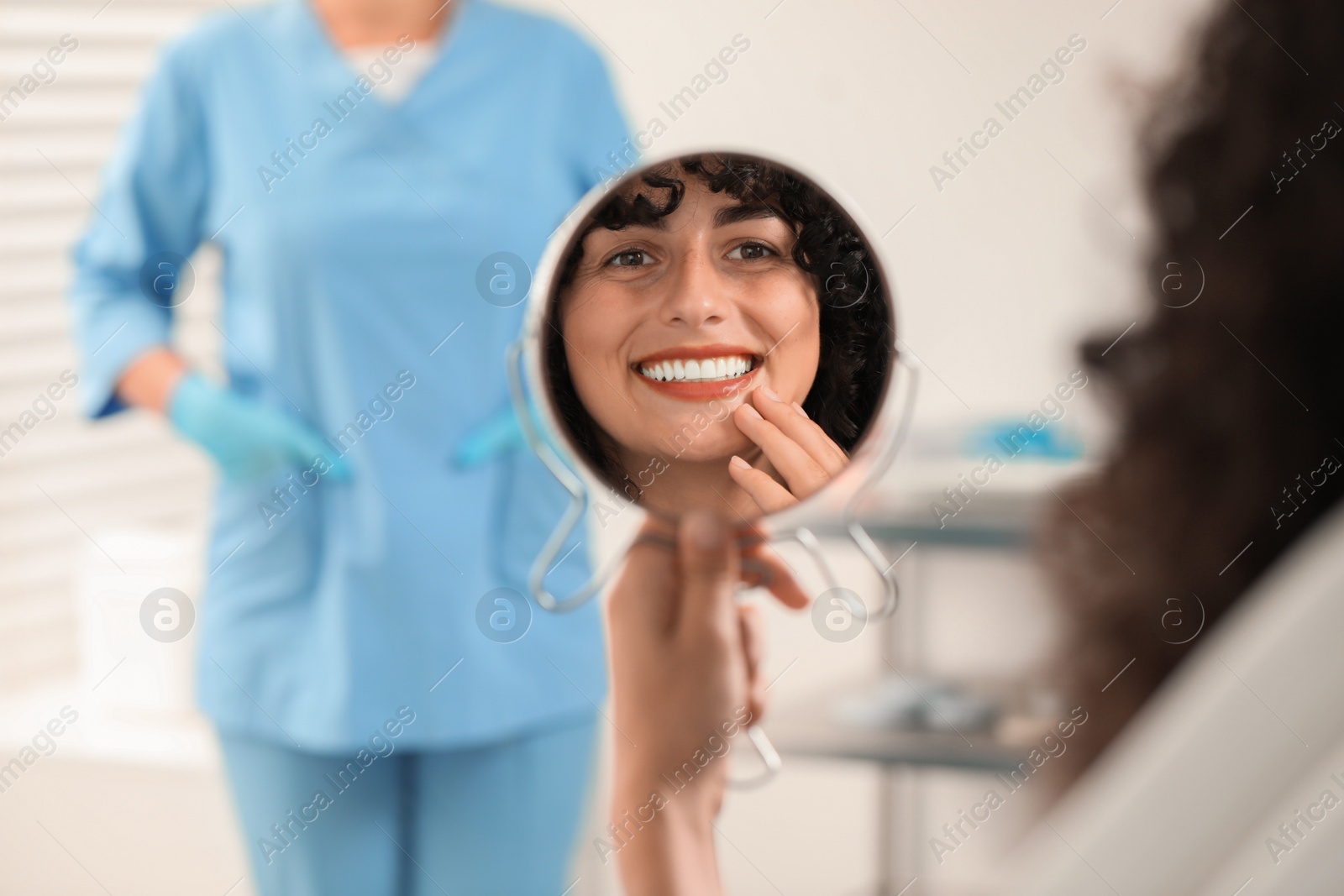 Photo of Patient looking in mirror and doctor in clinic, selective focus. Dental veneers