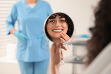 Photo of Patient looking in mirror and doctor in clinic, selective focus. Dental veneers