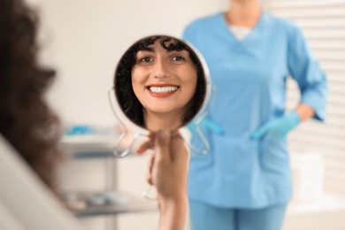 Photo of Patient looking in mirror and doctor in clinic, selective focus. Dental veneers