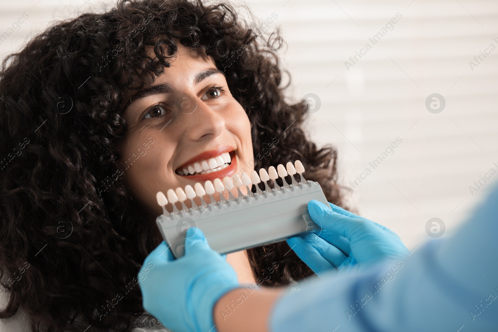 Photo of Doctor checking young woman's teeth color in clinic, closeup. Dental veneers