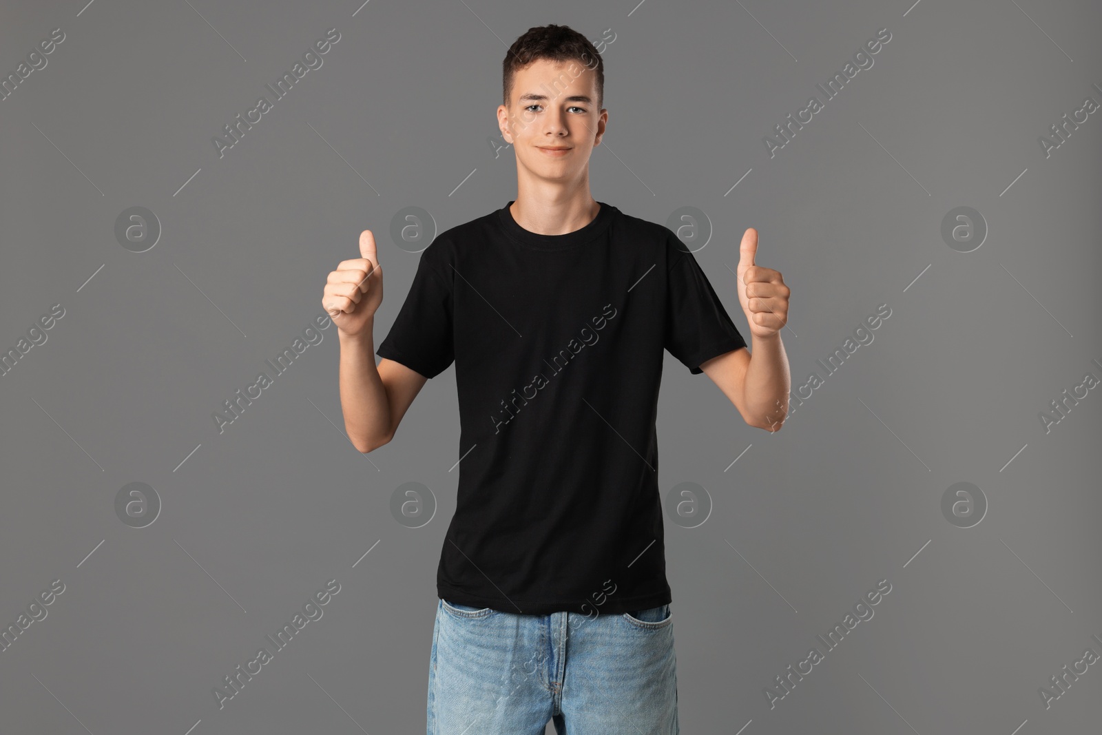 Photo of Teenage boy wearing black t-shirt and showing thumbs up on grey background