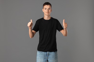 Teenage boy wearing black t-shirt and showing thumbs up on grey background