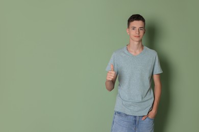 Photo of Teenage boy wearing light grey t-shirt and showing thumbs up on green background, space for text