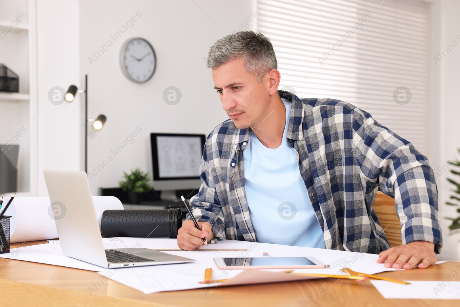 Photo of Architect making engineering drawing at wooden table in office