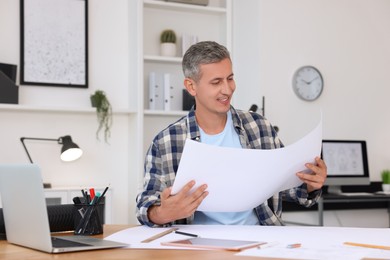 Architect checking engineering drawing at table in office