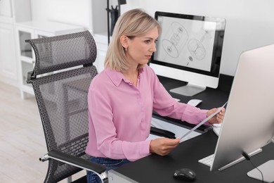 Architect with engineering drawing at table in office