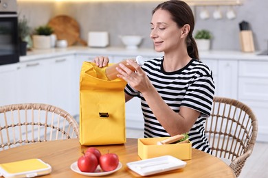 Smiling woman preparing lunch box with healthy snacks at wooden table in kitchen