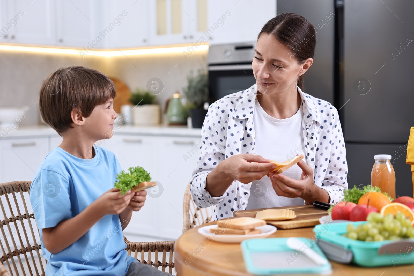 Photo of Mother and her cute son preparing lunch box with healthy food at wooden table in kitchen