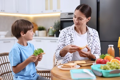 Mother and her cute son preparing lunch box with healthy food at wooden table in kitchen