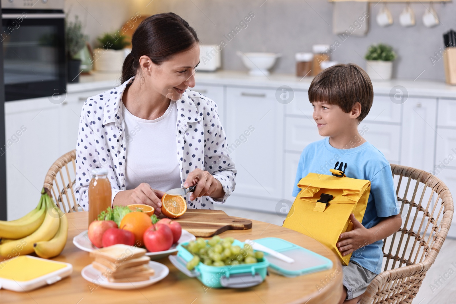 Photo of Mother and her cute son preparing lunch box with healthy food at wooden table in kitchen