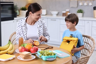 Photo of Mother and her cute son preparing lunch box with healthy food at wooden table in kitchen