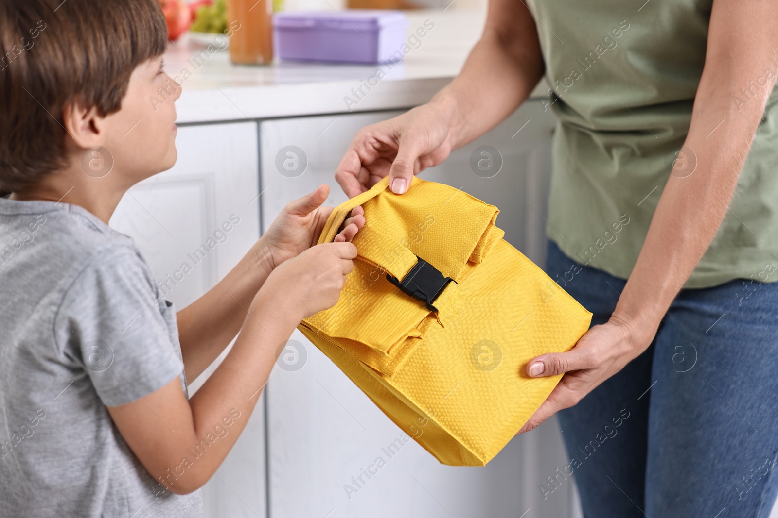 Photo of Mother giving lunch bag to her son in kitchen, closeup