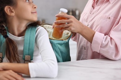 Mother putting bottle of drink into daughter`s backpack in kitchen, closeup. Preparing for school