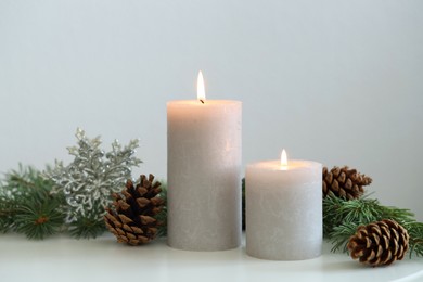 Photo of Burning candles and fir branches on white table. Christmas atmosphere