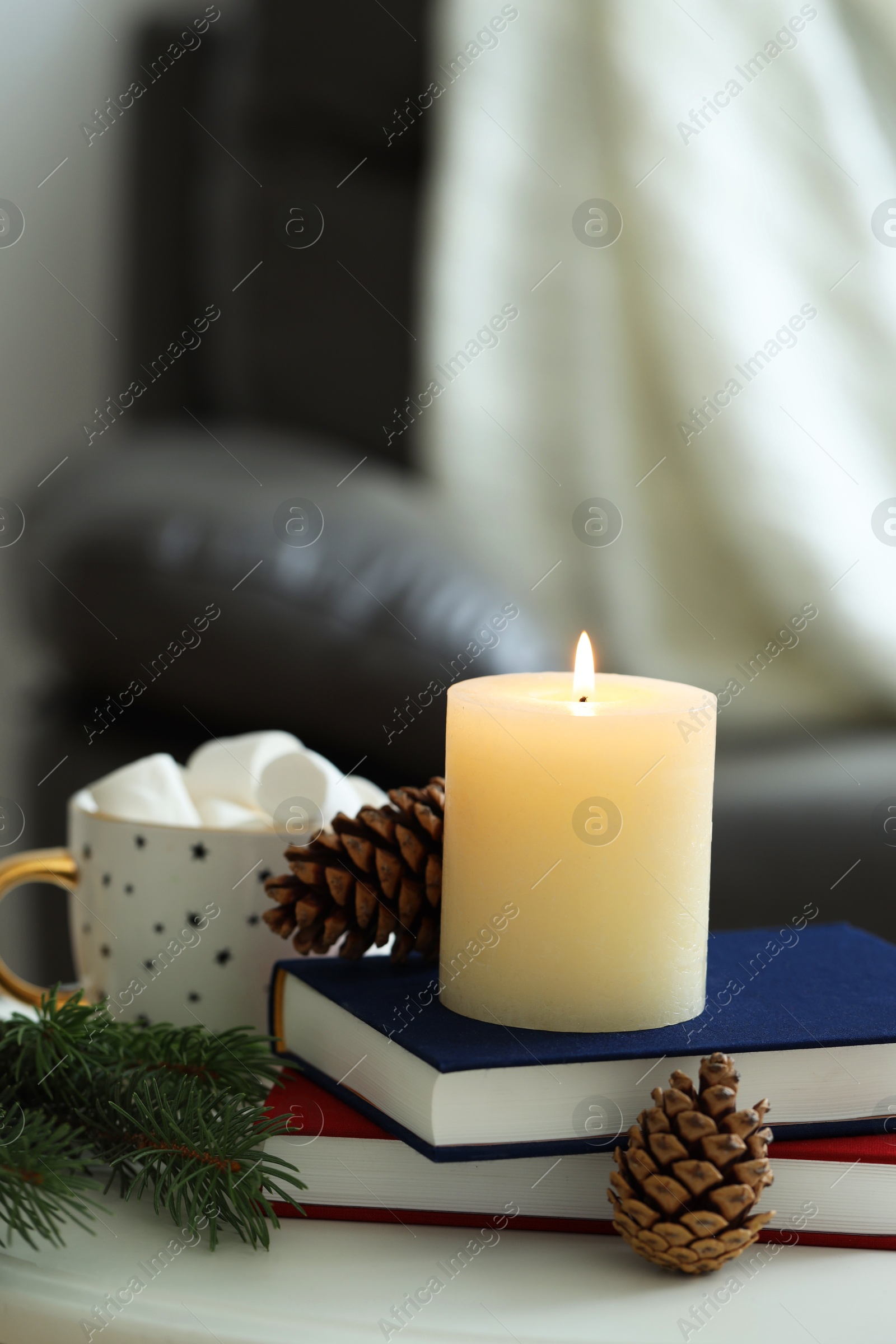 Photo of Burning candle, books, fir branches and cones on coffee table indoors, space for text. Christmas atmosphere