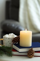 Photo of Burning candle, books, fir branches and cones on coffee table indoors, space for text. Christmas atmosphere