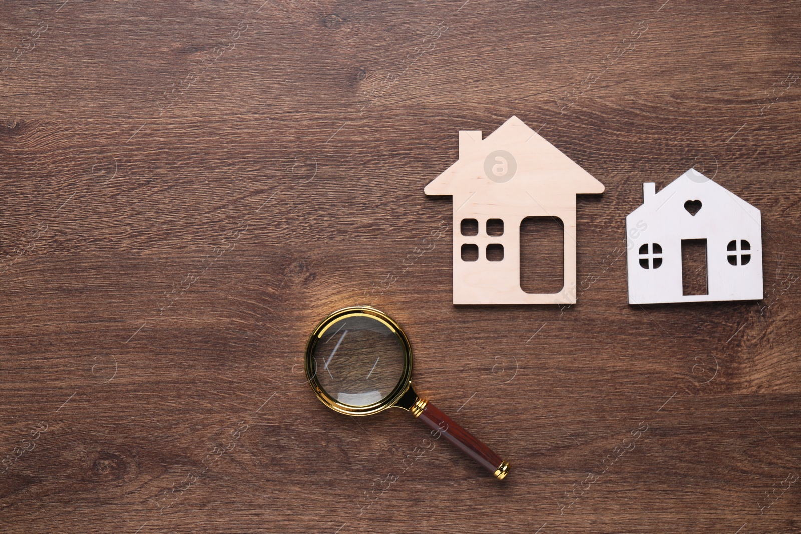 Photo of House hunting. Magnifying glass and house figures on wooden background, flat lay. Space for text