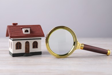 House hunting. Magnifying glass and house model on wooden table