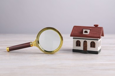 Photo of House hunting. Magnifying glass and house model on wooden table