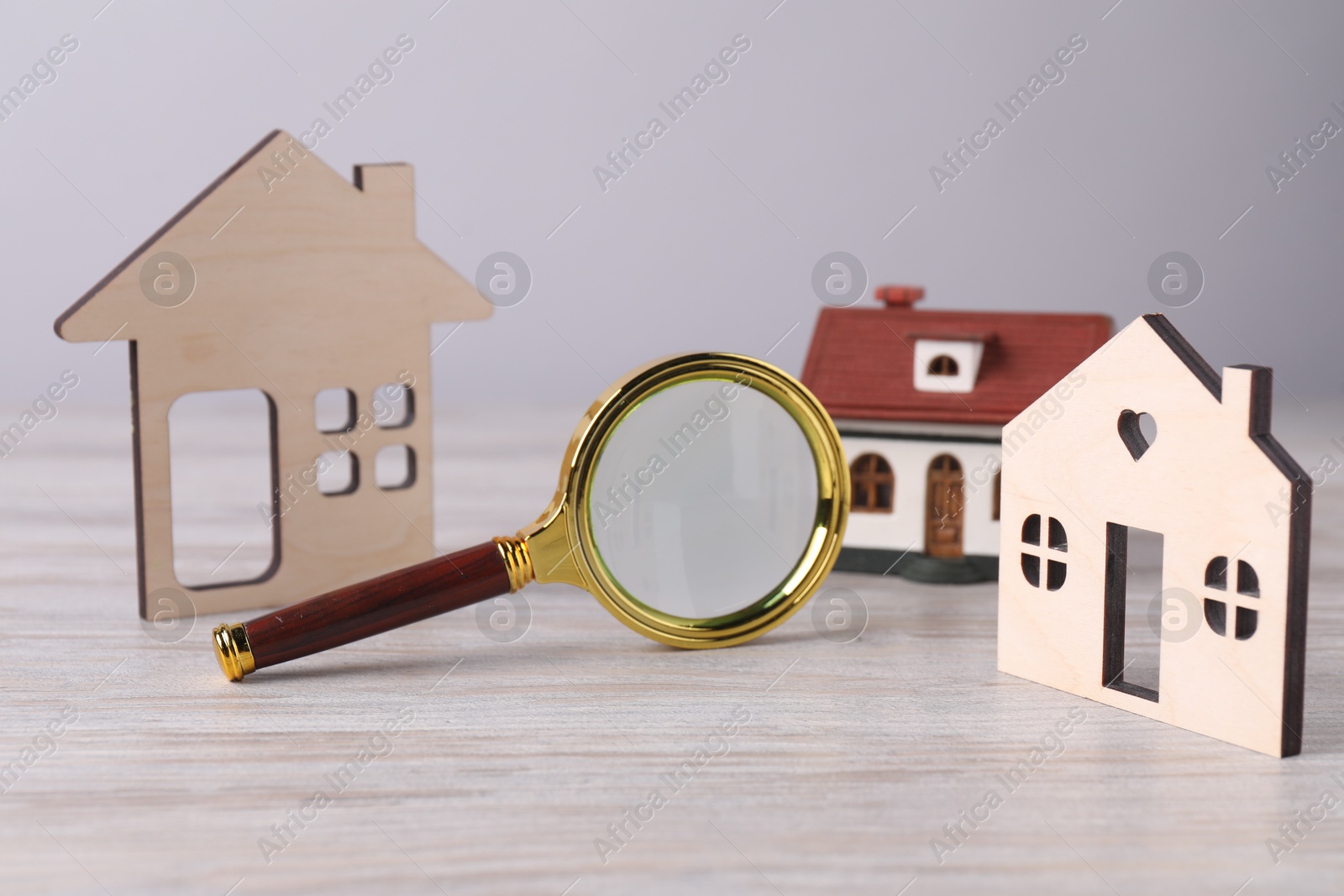 Photo of House hunting. Magnifying glass and house figures on wooden table