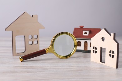 House hunting. Magnifying glass and house figures on wooden table