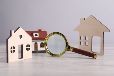 Photo of House hunting. Magnifying glass and house figures on wooden table