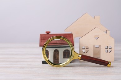 Photo of House hunting. Magnifying glass and house figures on wooden table