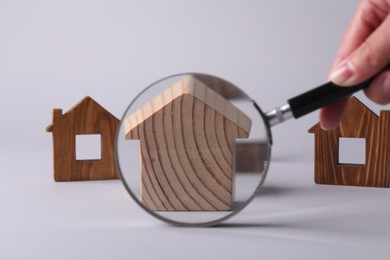 Photo of House hunting. Woman with magnifying glass and house figure on grey background, closeup