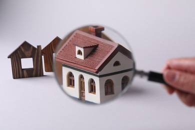 Photo of House hunting. Woman with magnifying glass and house figure on grey background, closeup