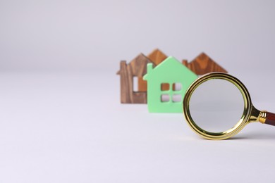 Photo of House hunting. Magnifying glass and house figures on grey background. Space for text