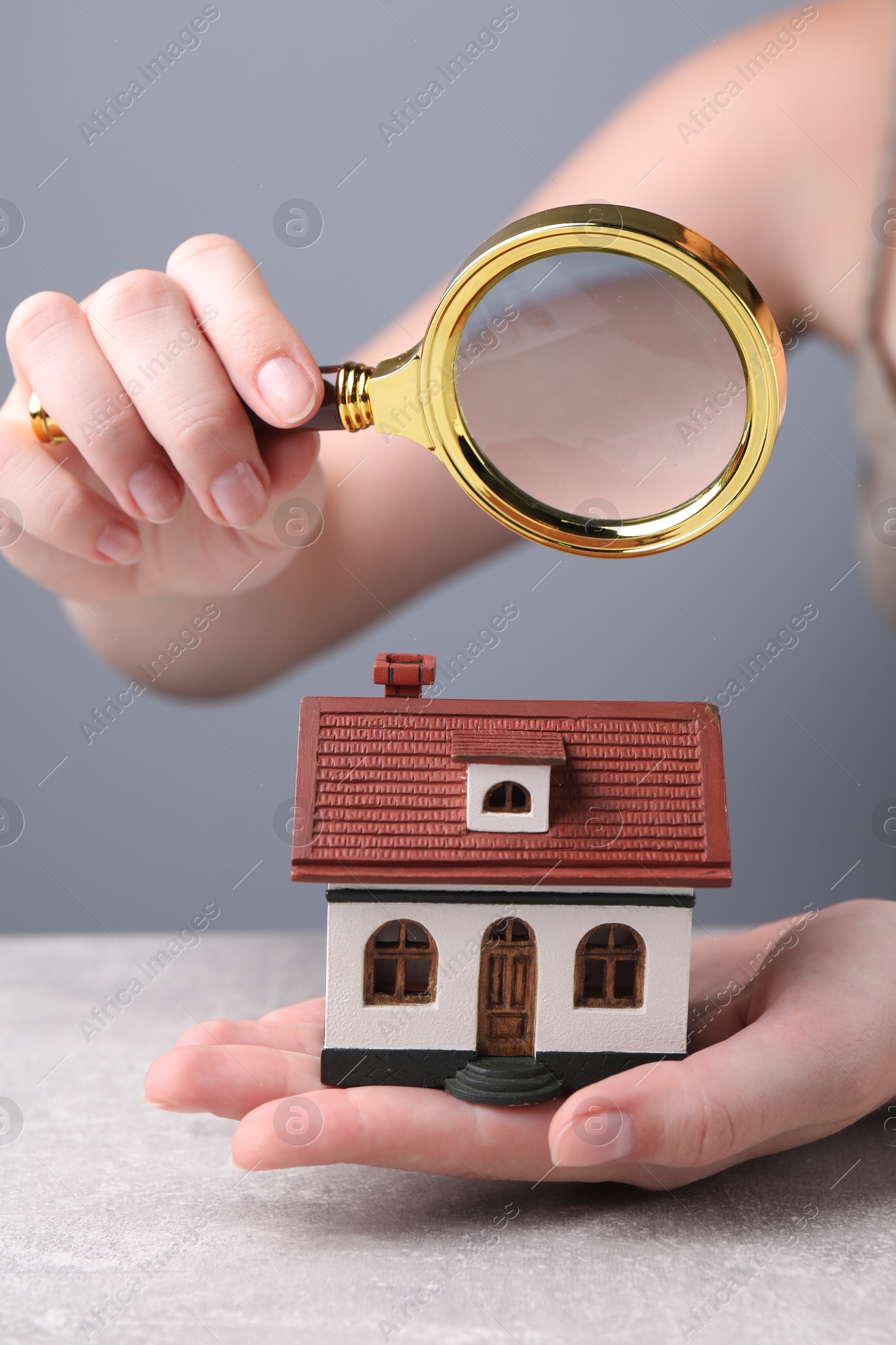 Photo of House hunting. Woman with magnifying glass and house model at grey table, closeup