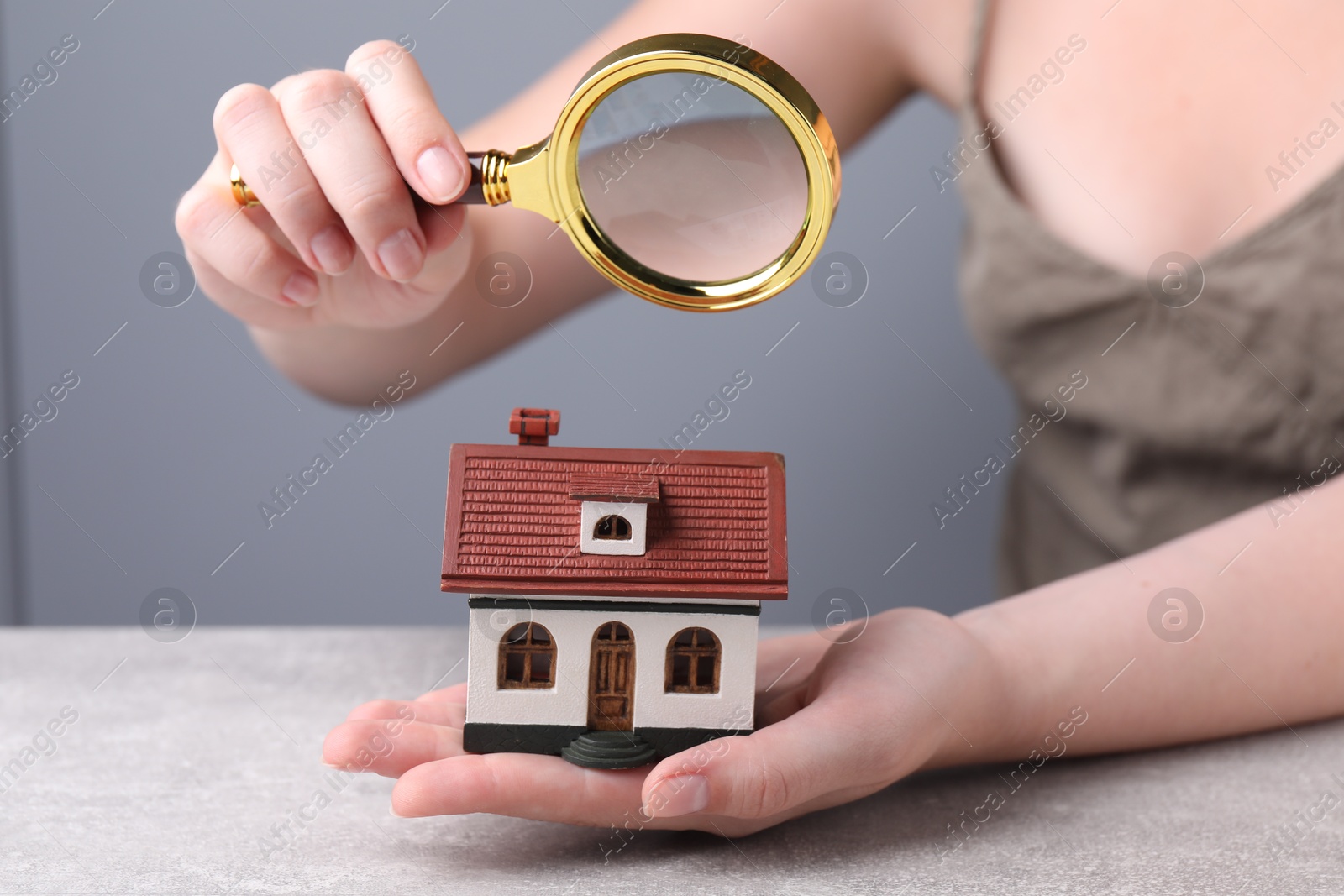 Photo of House hunting. Woman with magnifying glass and house model at grey table, closeup