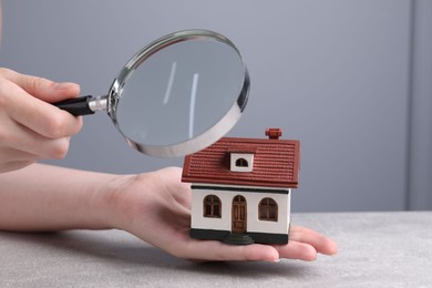 Photo of House hunting. Woman with magnifying glass and house model at grey table, closeup