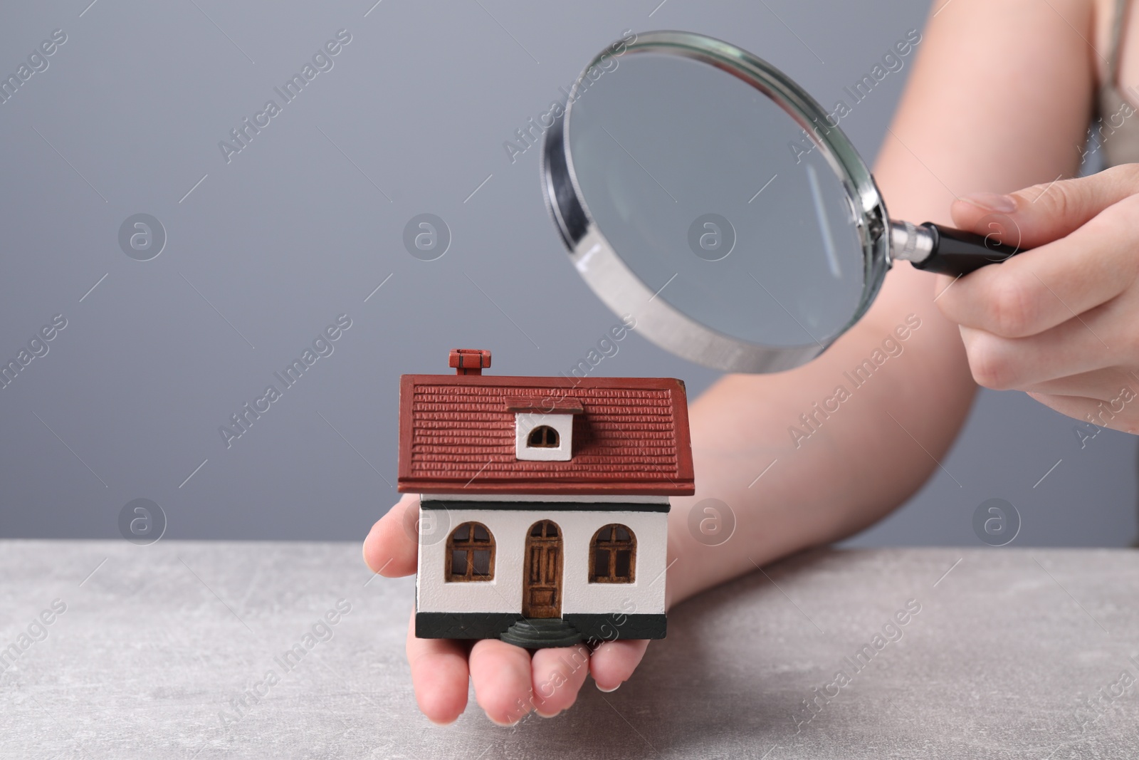 Photo of House hunting. Woman with magnifying glass and house model at grey table, closeup