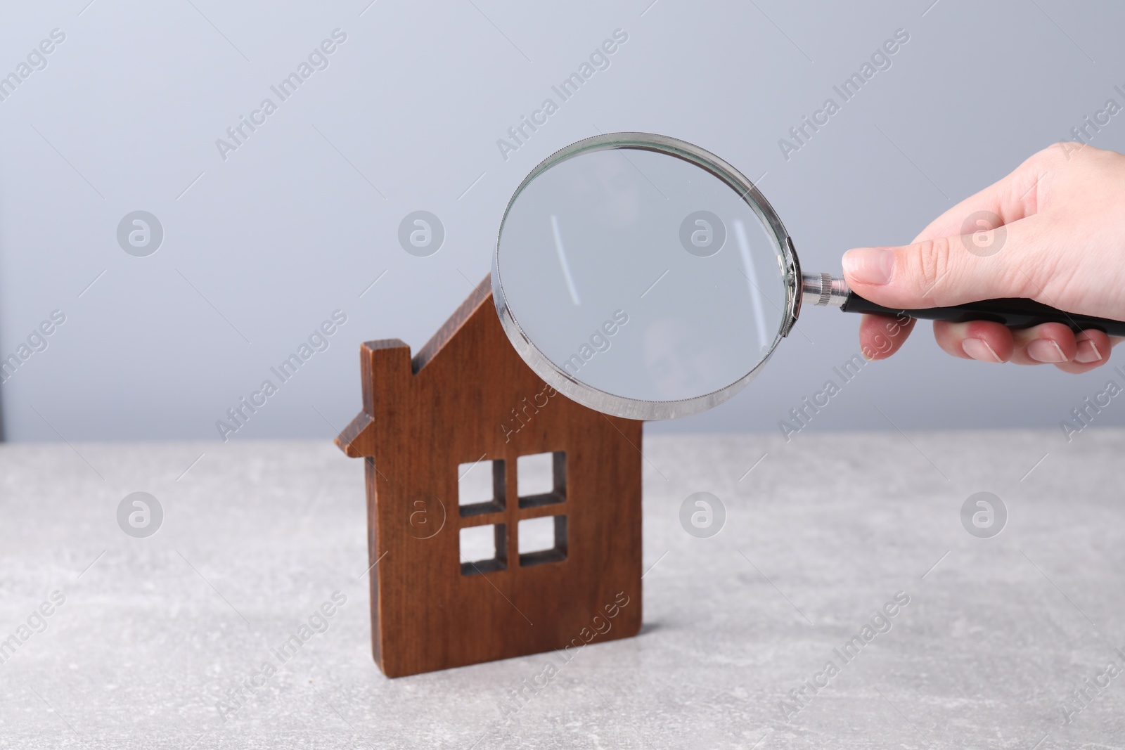 Photo of House hunting. Woman with magnifying glass and house figure at grey table, closeup