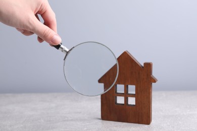 Photo of House hunting. Woman with magnifying glass and house figure at grey table, closeup