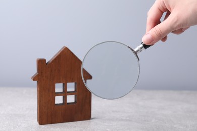 House hunting. Woman with magnifying glass and house figure at grey table, closeup