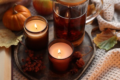 Photo of Burning candles, freshly brewed tea and autumn decor on fabric, closeup