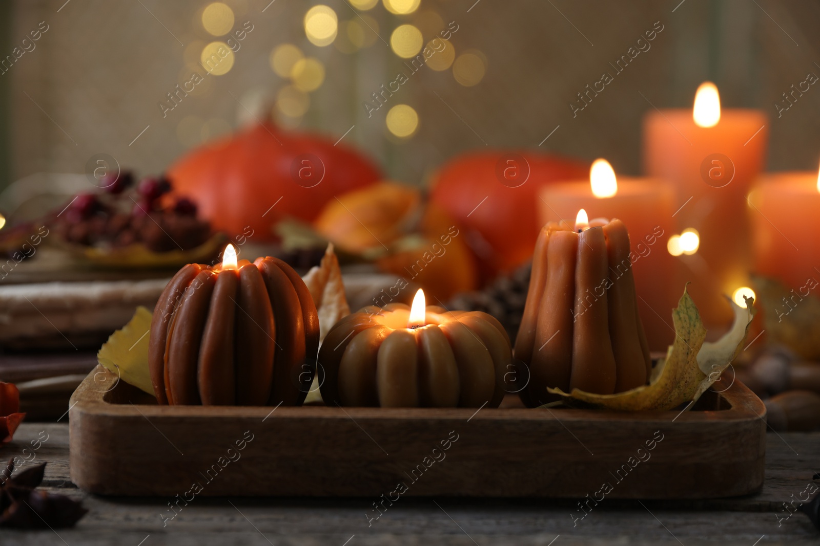 Photo of Burning candles in shape of pumpkins and autumn decor on wooden table